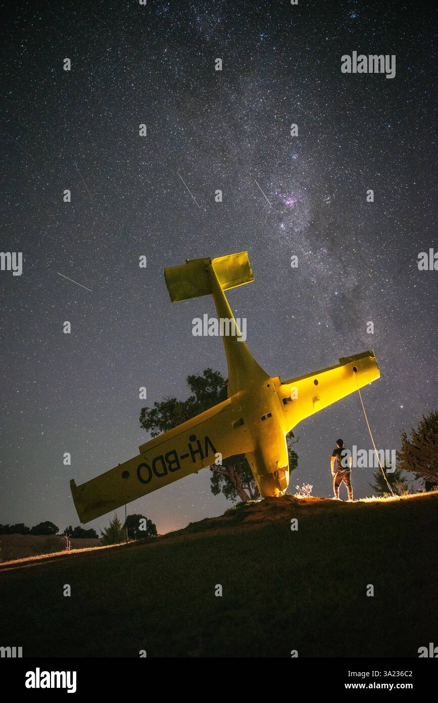 personne avec la lumière debout à côté de l'avion jaune la nuit et étoiles filantes avec Banque D'Images