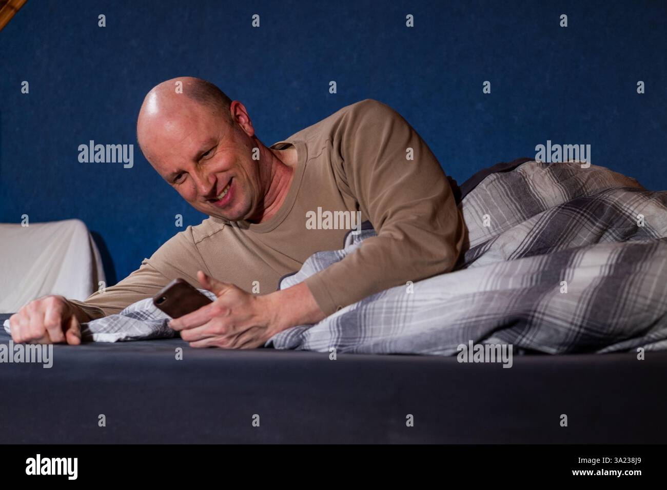 Homme au lit, regardant sur un appareil mobile. Banque D'Images