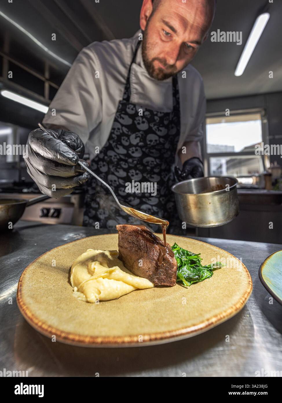 Chef versant de la sauce sur un plat de viande grillée avec purée de pommes de terre et épinards Banque D'Images
