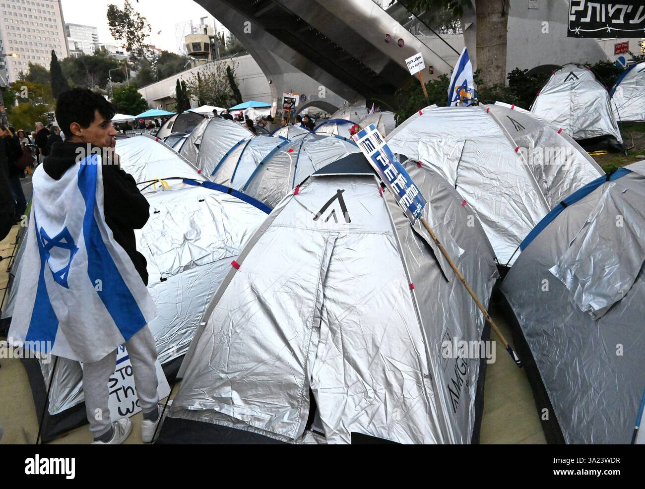 Tel Aviv, États-Unis. 11 mars 2025. Un homme porte un drapeau israélien devant un campement de tente de protestation devant le ministère israélien de la Défense à tel Aviv, appelant le premier ministre israélien Benjamin Netanyahu à entrer dans la deuxième phase de l’accord de cessez-le-feu et la libération des otages détenus par le Hamas à Gaza le mardi 11 mars 2025. Photo de Debbie Hill/ crédit : UPI/Alamy Live News Banque D'Images