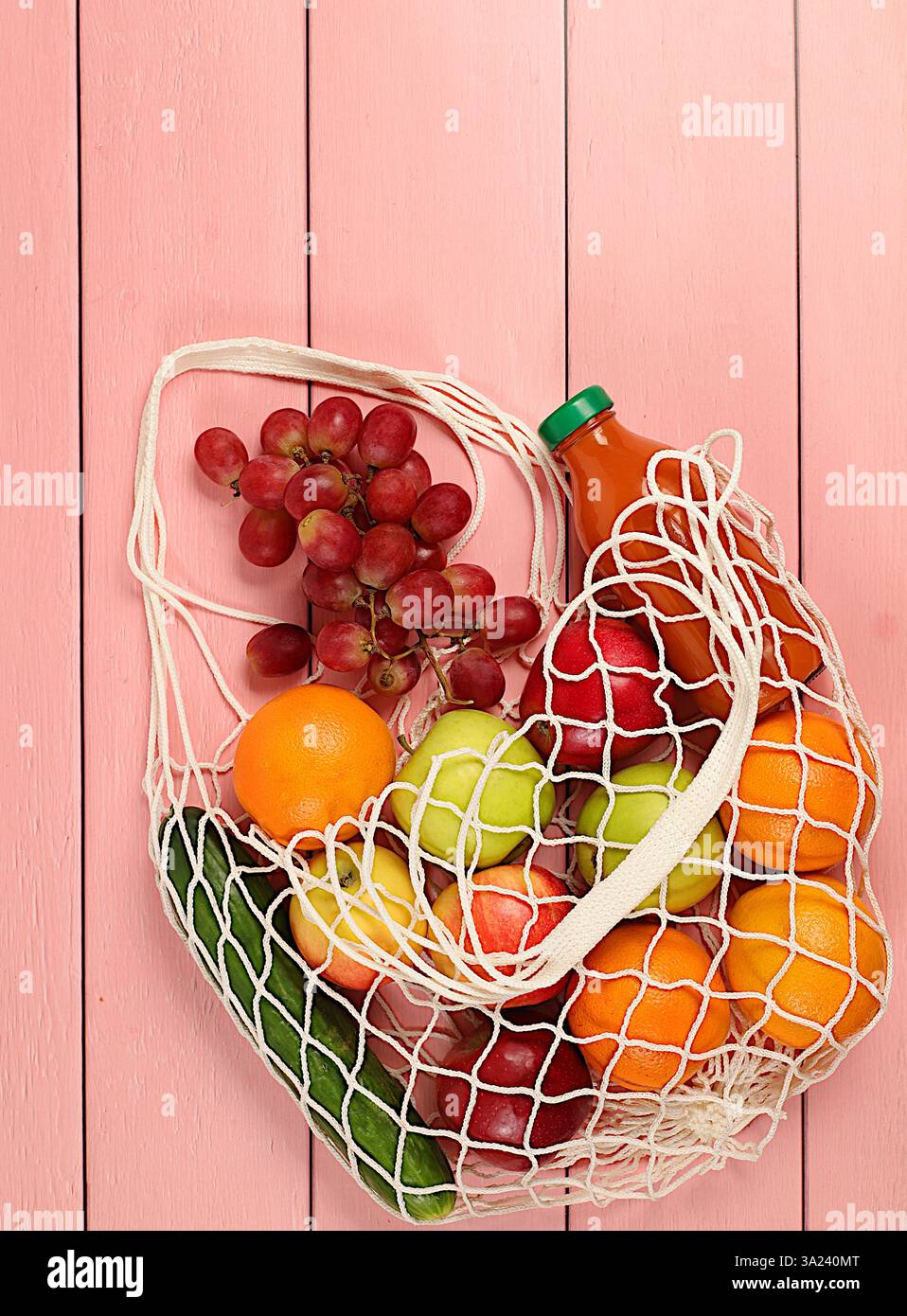 Raisins, oranges, tomates, pommes, bananes et jus naturel dans un sac en coton sur un fond en bois, concept de livraison de nourriture, sac de ficelle en tissu avec un v. Banque D'Images