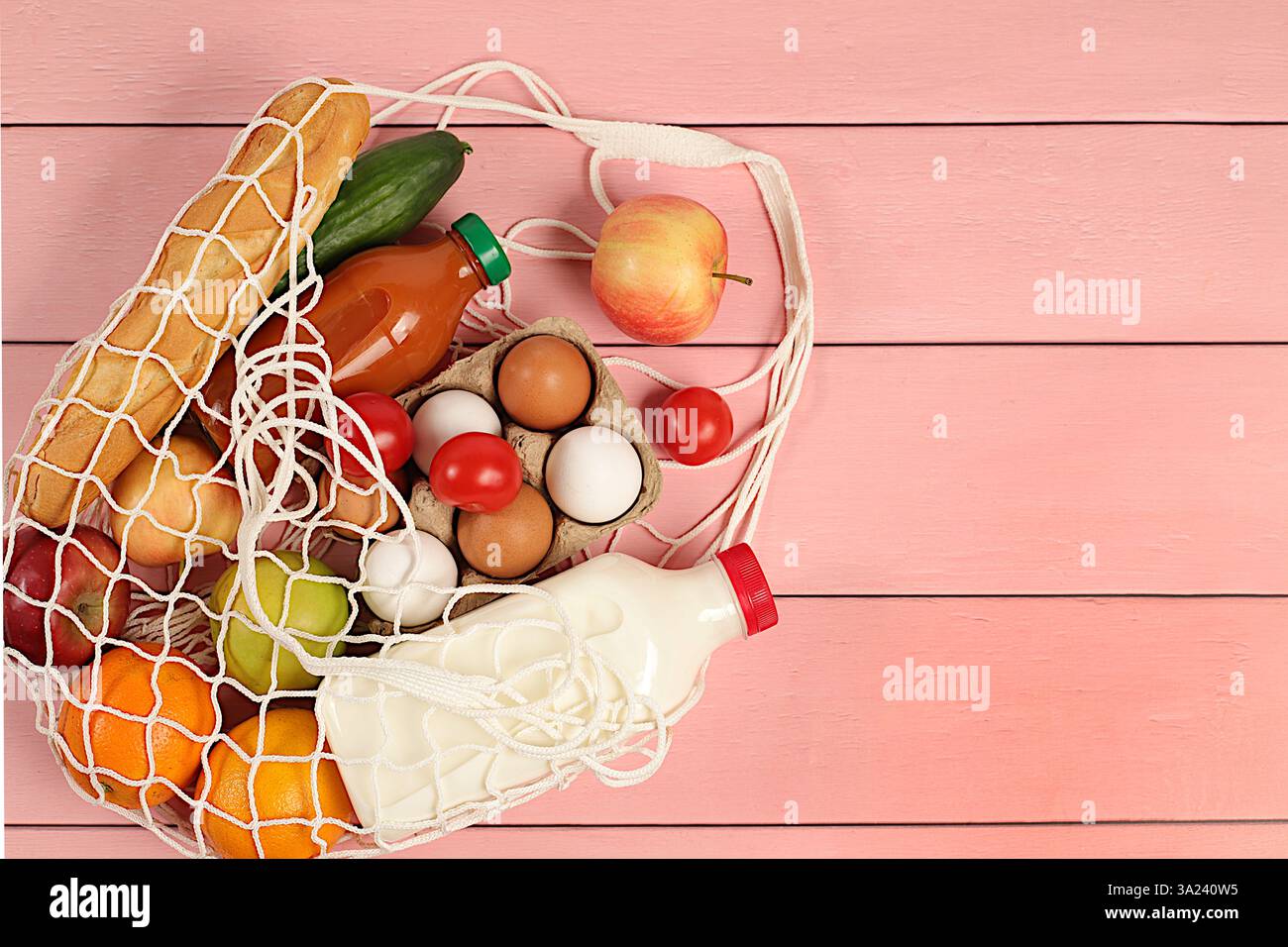 Sac de corde en tissu avec divers produits naturels. Lait, œufs, baguettes, jus naturel et fruits dans un sac en coton sur fond de bois, livraison de nourriture Banque D'Images