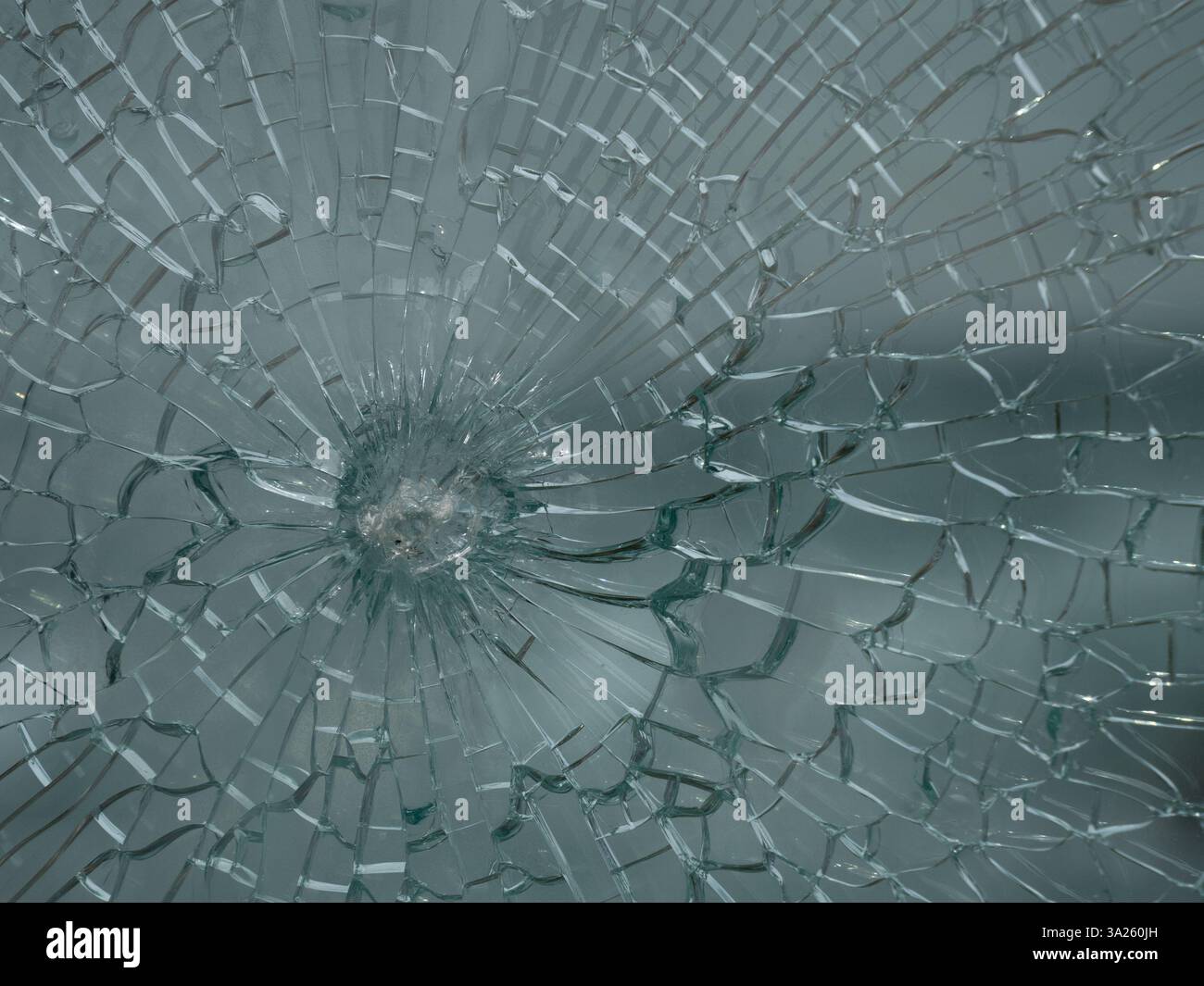 Gros plan d'une vitre fissurée présentant un motif radial. Le verre de sécurité se fissure, mais les intercalaires en plastique maintiennent les éclats ensemble. Banque D'Images