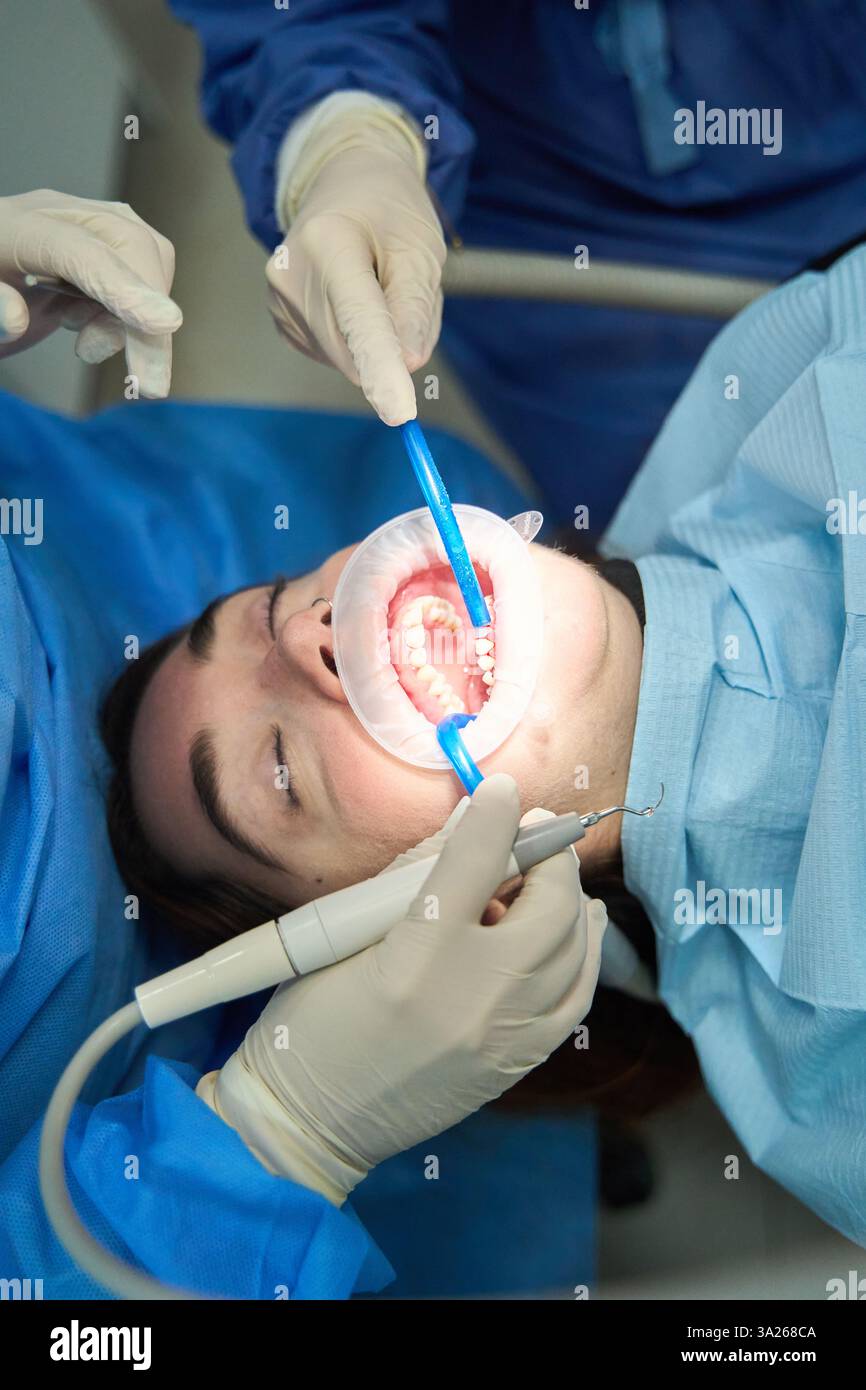 Équipe dentaire travaillant sur la bouche d'un patient à l'aide d'outils spécialisés, réalisant une intervention dentaire Banque D'Images Équipe dentaire travaillant sur la bouche d'un patient à l'aide d'outils spécialisés, réalisant une intervention dentaire Banque D'Images