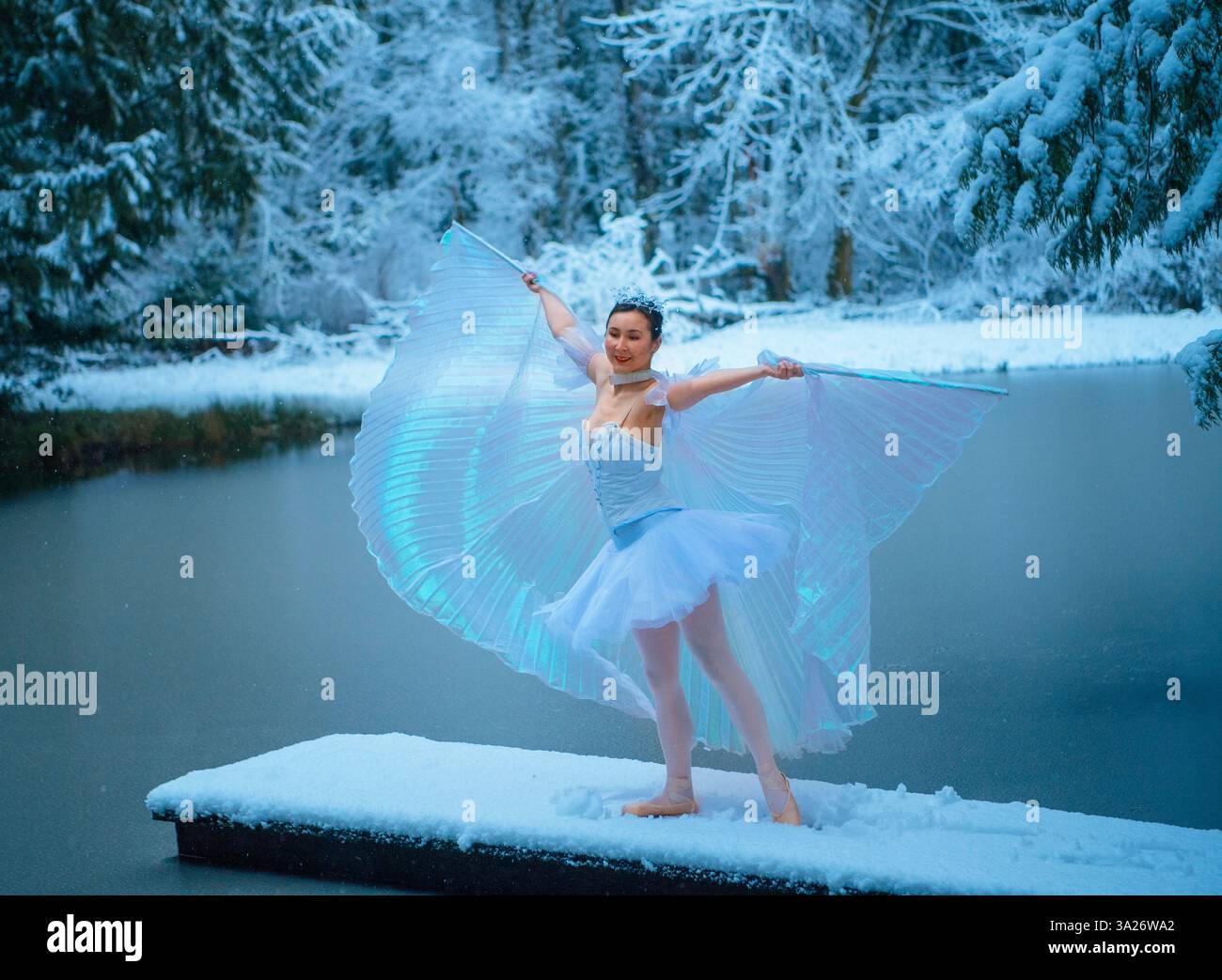 Femme en costume blanc élégant dansant sur la jetée couverte de neige à côté du lac d'hiver. WA, ÉTATS-UNIS Banque D'Images