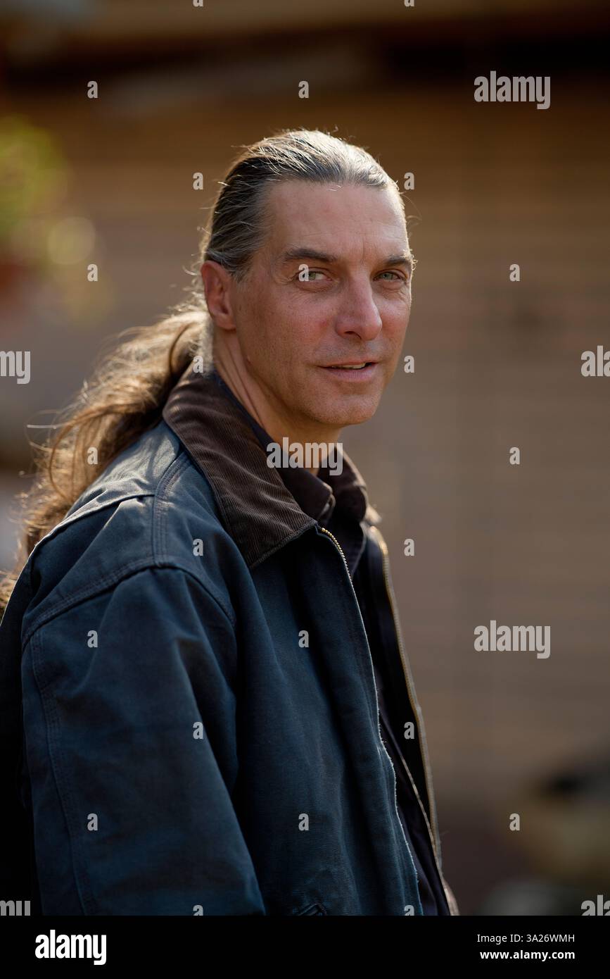 Homme aux cheveux longs et veste en denim debout à l'extérieur avec un fond flou. Brandebourg, Allemagne Banque D'Images