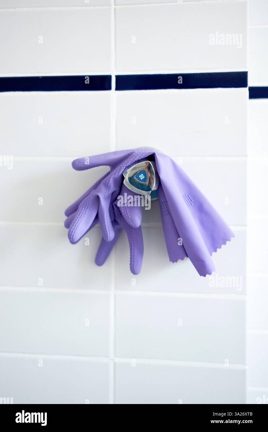 Des gants de nettoyage violets sont suspendus à un mur carrelé blanc avec une bande accentuée bleue. Berlin, Allemagne Banque D'Images
