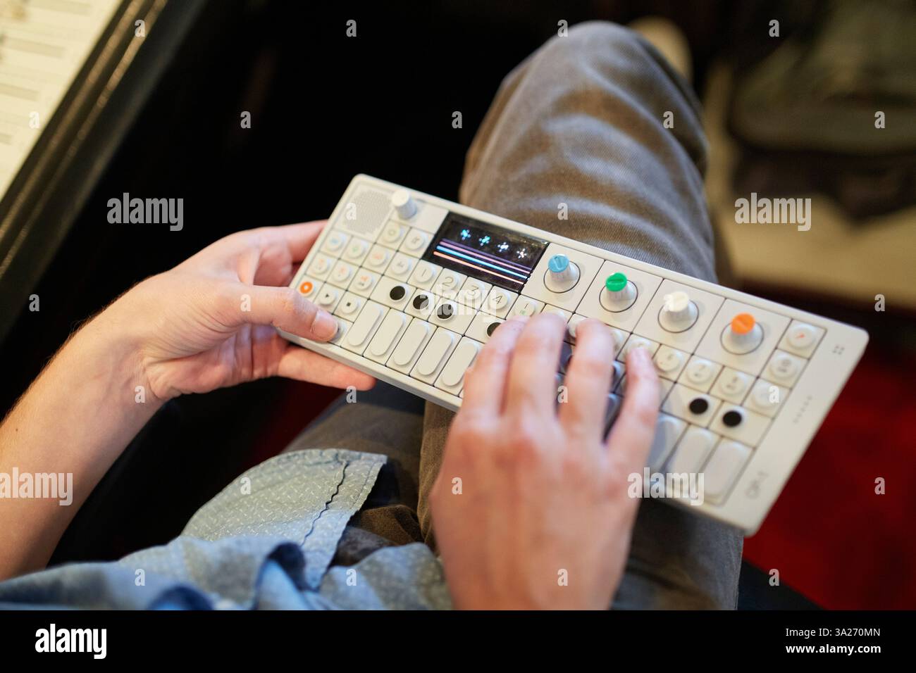 Mains jouant un synthétiseur électronique compact avec des boutons colorés sur les genoux d'une personne dans un studio d'enregistrement. Banque D'Images