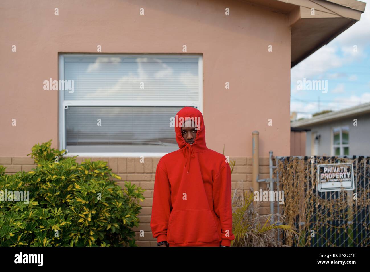 Jeune homme en sweat à capuche rouge se tient devant une maison de pêche avec une fenêtre et des plantes. Miami, Floride Banque D'Images