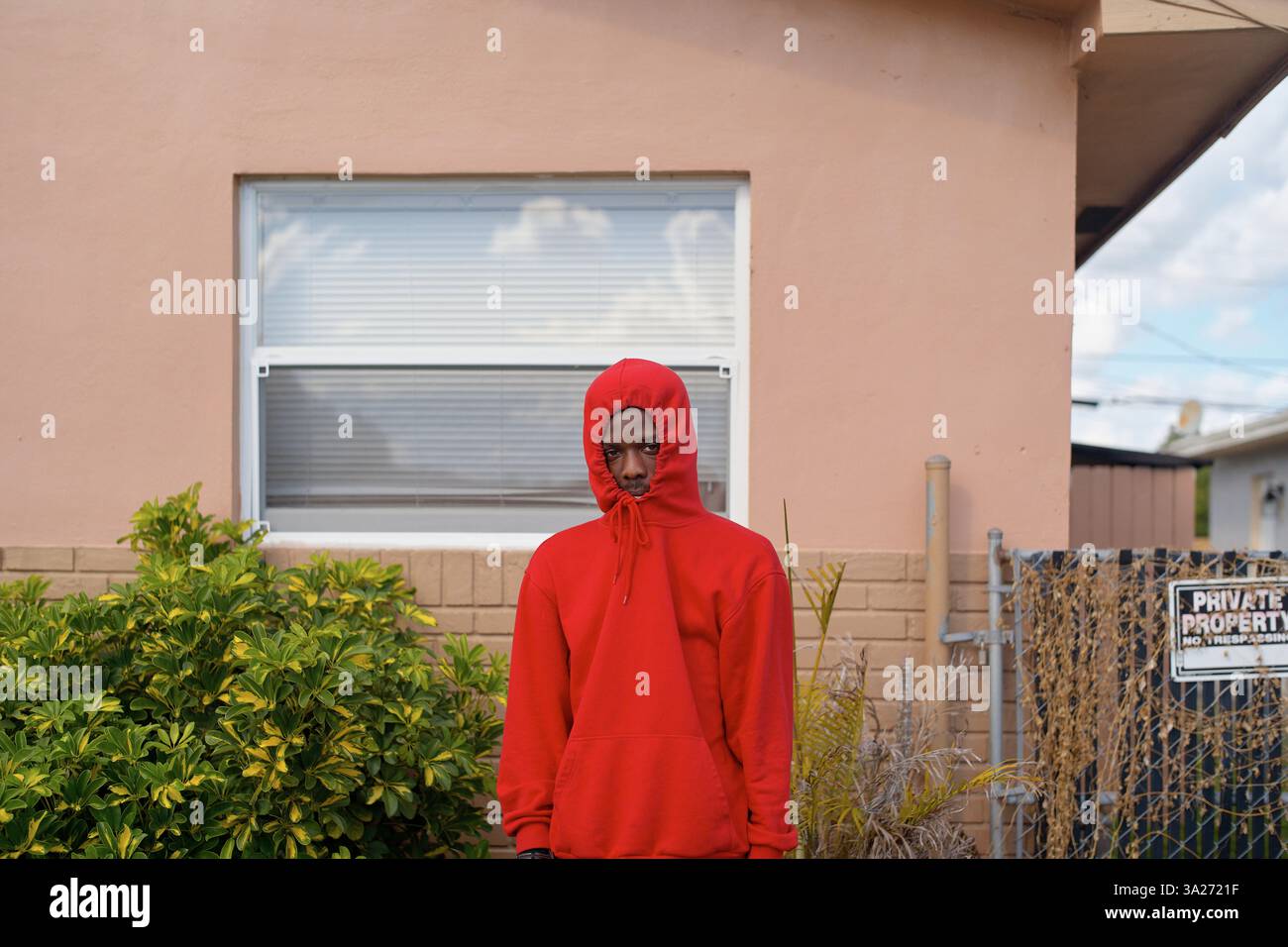 Jeune homme en sweat à capuche rouge se tient devant une maison de pêche avec une fenêtre et des plantes. Miami, Floride Banque D'Images