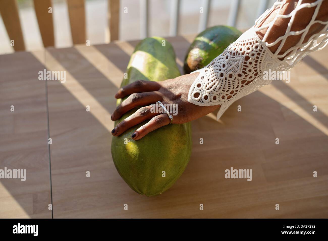 Main élégante avec anneau sur de grandes papayes vertes sur une table en bois à la lumière du soleil. Miami, Floride, États-Unis Banque D'Images