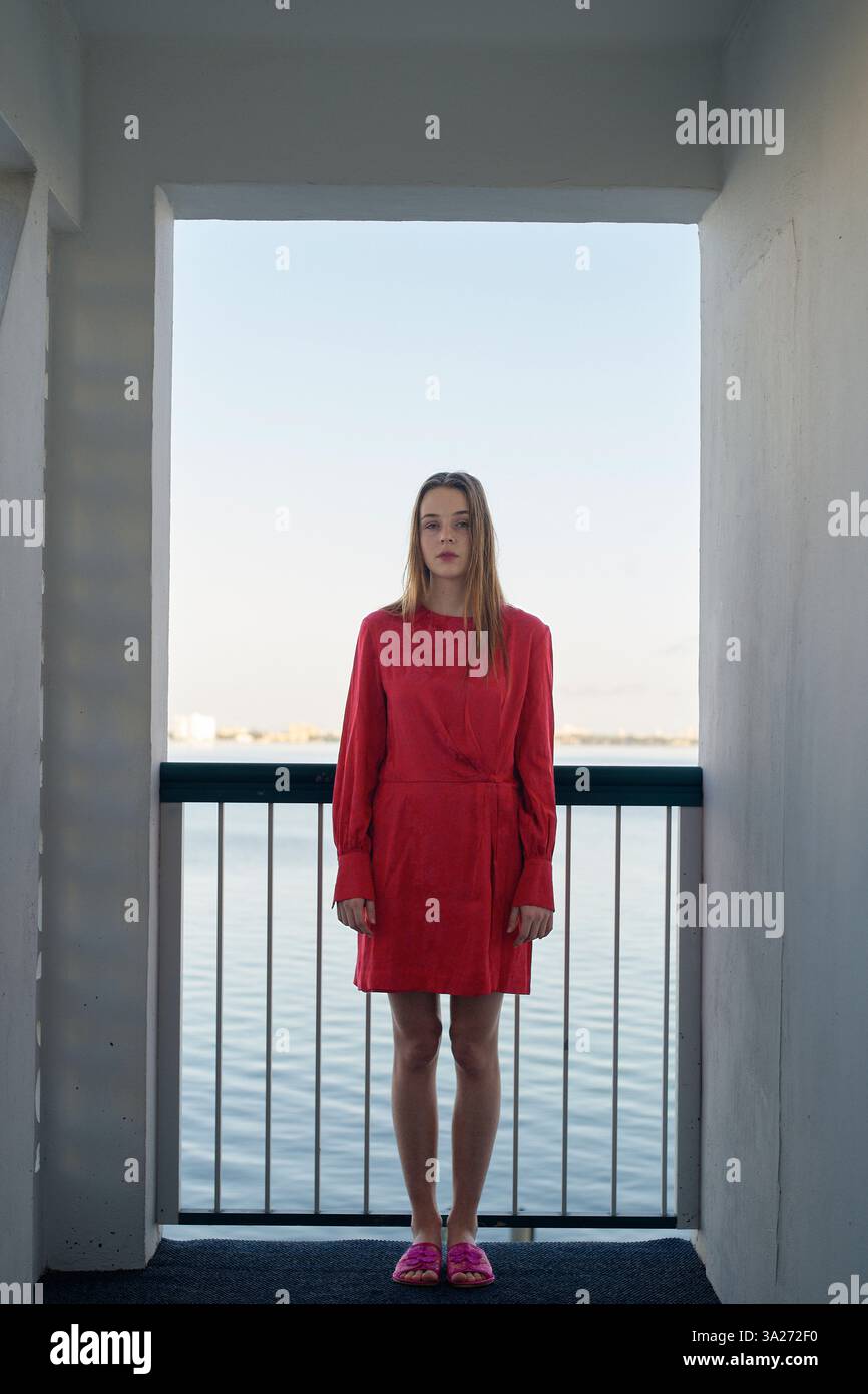 Femme en robe rouge debout dans une porte avec une vue sur l'eau sereine en arrière-plan. Miami, Floride, États-Unis Banque D'Images