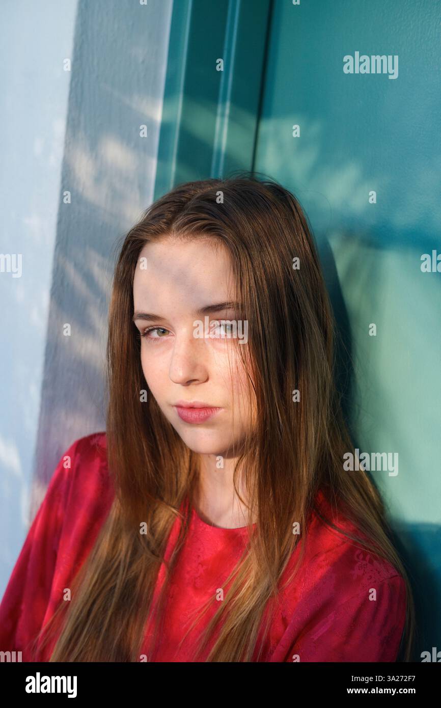 Jeune femme en haut rouge contre un mur sarcelle avec des motifs d'ombre sur son visage. Miami, Floride, États-Unis Banque D'Images