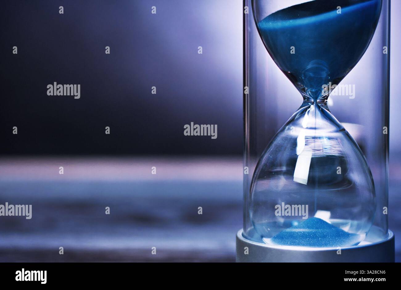 Sable bleu s'écoulant à travers le sablier mesurant le temps de passage. Un arrière-plan sombre avec espace de copie Banque D'Images
