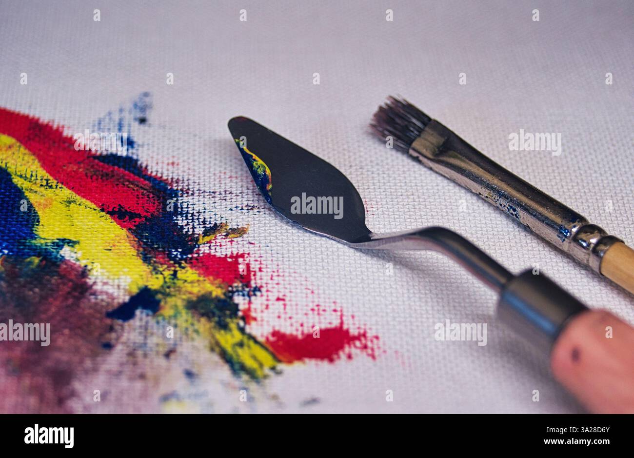 Couteau à palette et pinceau sur une toile avec des coups de peinture à l'huile colorés, incarnant le processus de création d'une œuvre d'art vibrante Banque D'Images