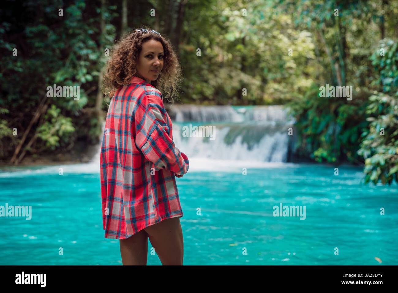 Femme magnifique sur la rivière turquoise dans la jungle avec cascade. Aventure tropicale avec femme regardant la caméra Banque D'Images