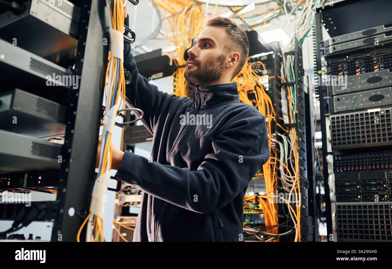 Vêtements noirs. Le jeune homme travaille avec des équipements Internet et des fils dans la salle des serveurs. Banque D'Images