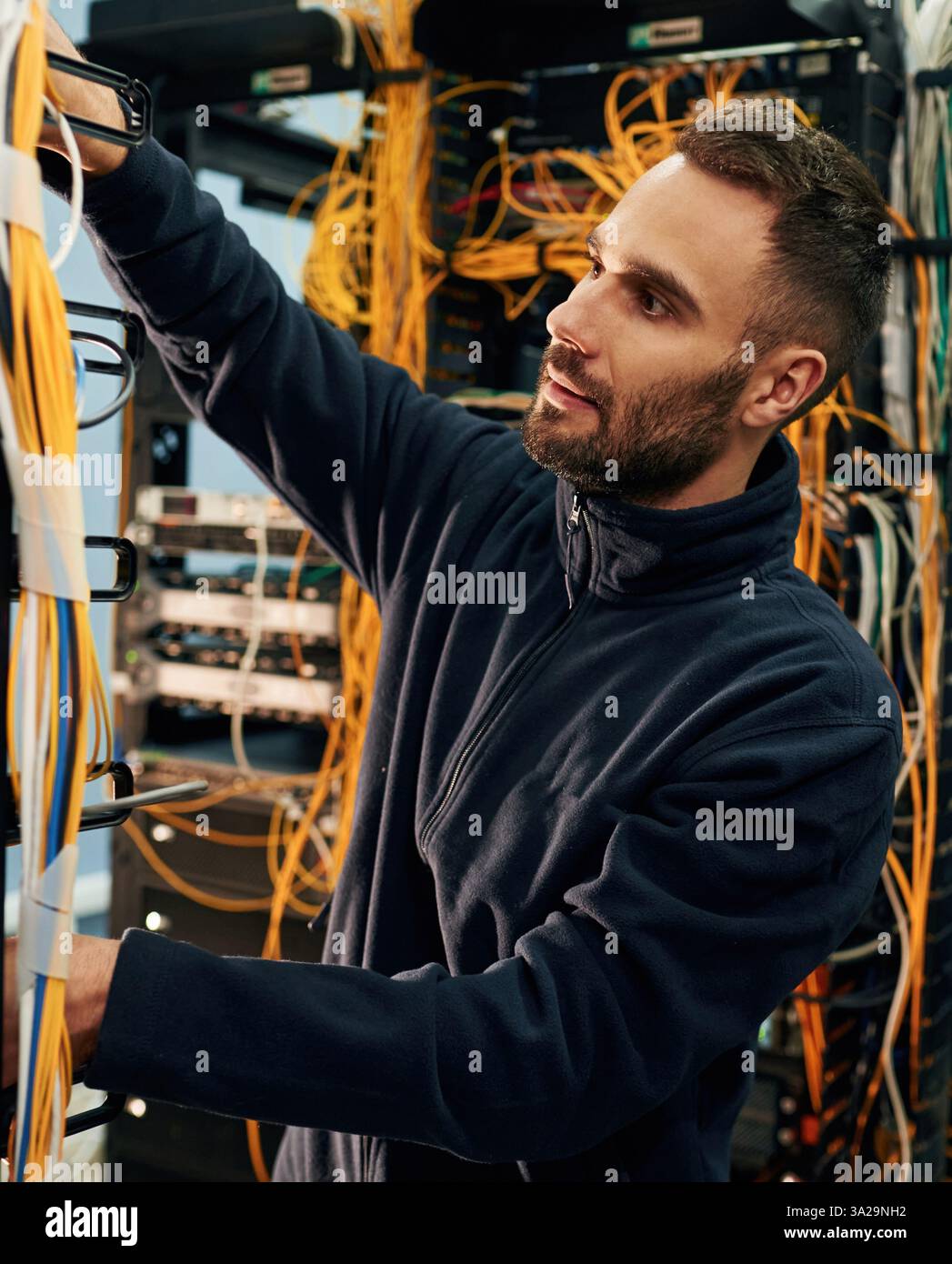 Vêtements noirs. Le jeune homme travaille avec des équipements Internet et des fils dans la salle des serveurs. Banque D'Images