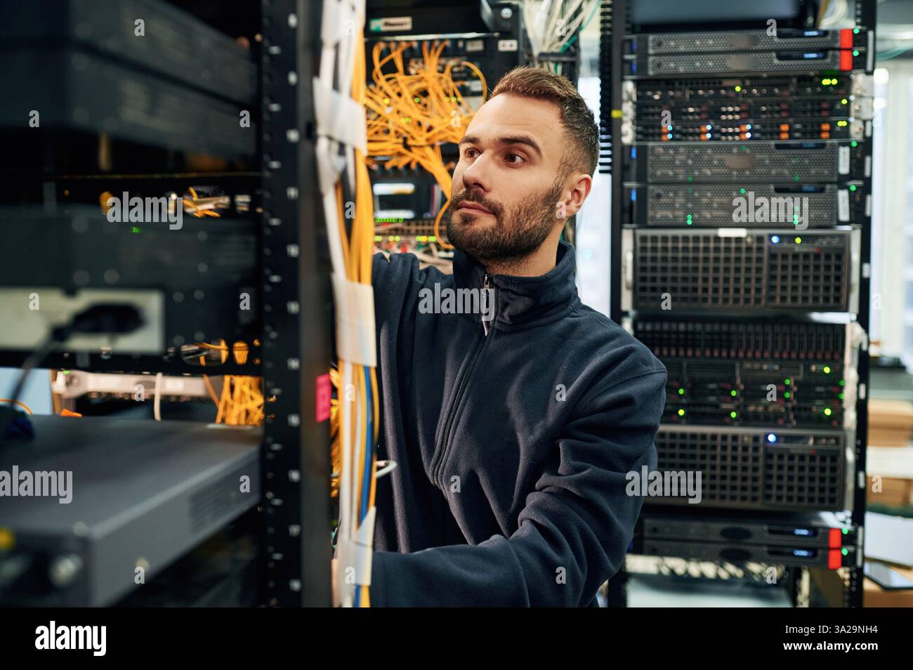 Vêtements noirs. Le jeune homme travaille avec des équipements Internet et des fils dans la salle des serveurs. Banque D'Images