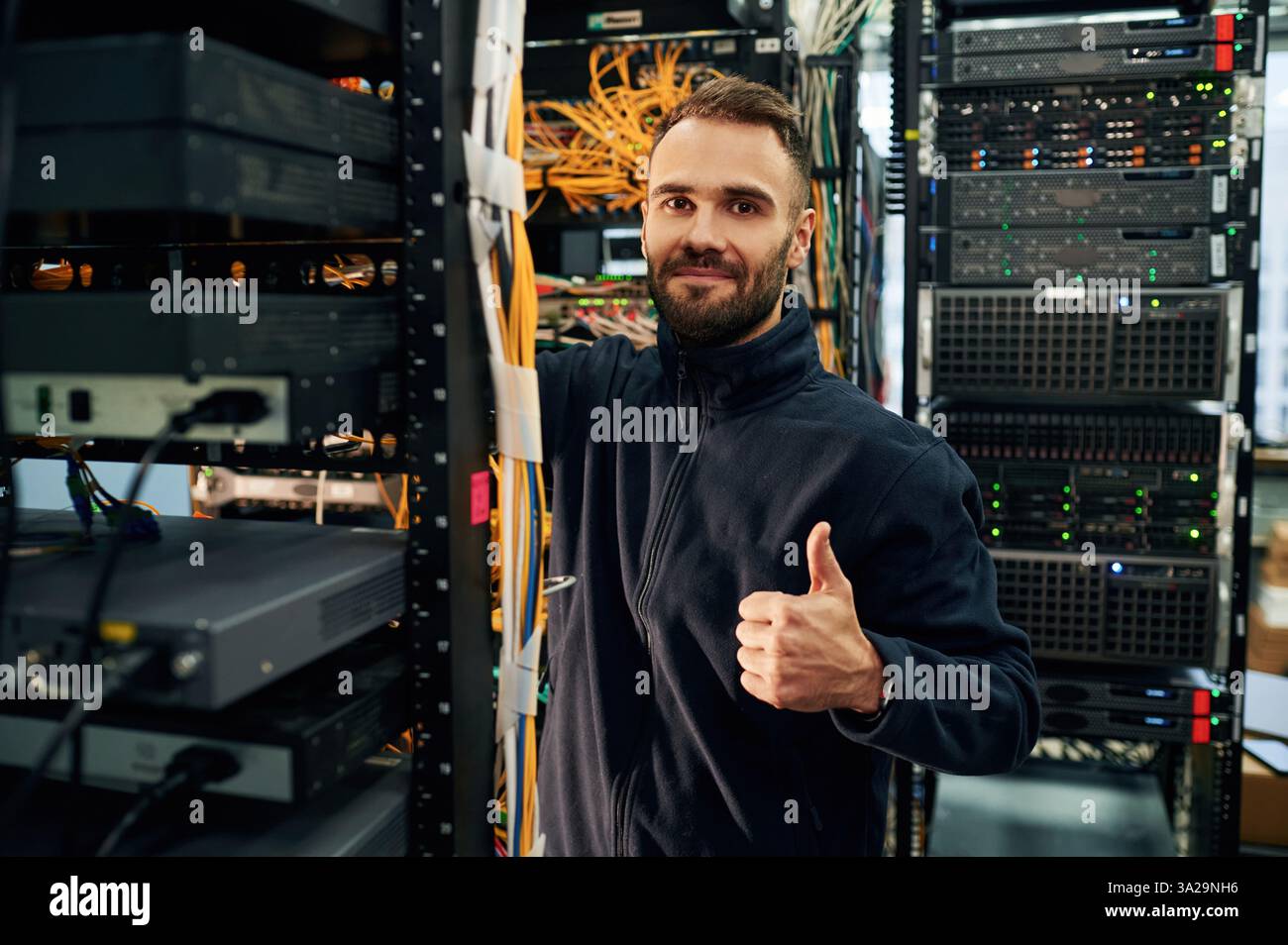 Vêtements noirs. Le jeune homme travaille avec des équipements Internet et des fils dans la salle des serveurs. Banque D'Images