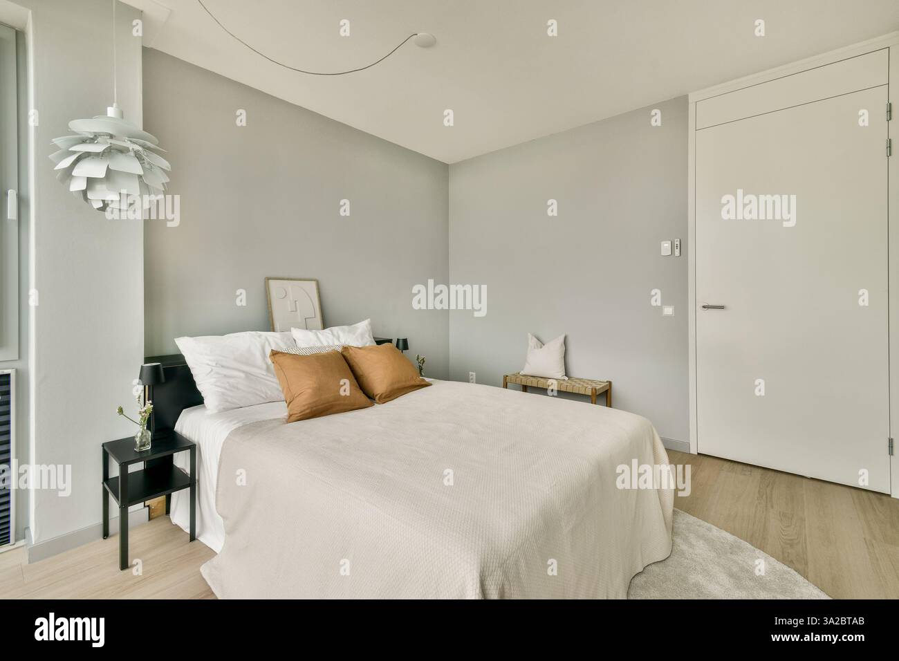 Cette chambre moderne et élégante présente une palette de couleurs neutres avec un lit, un décor élégant et une lumière naturelle inondée par de grandes fenêtres. Banque D'Images