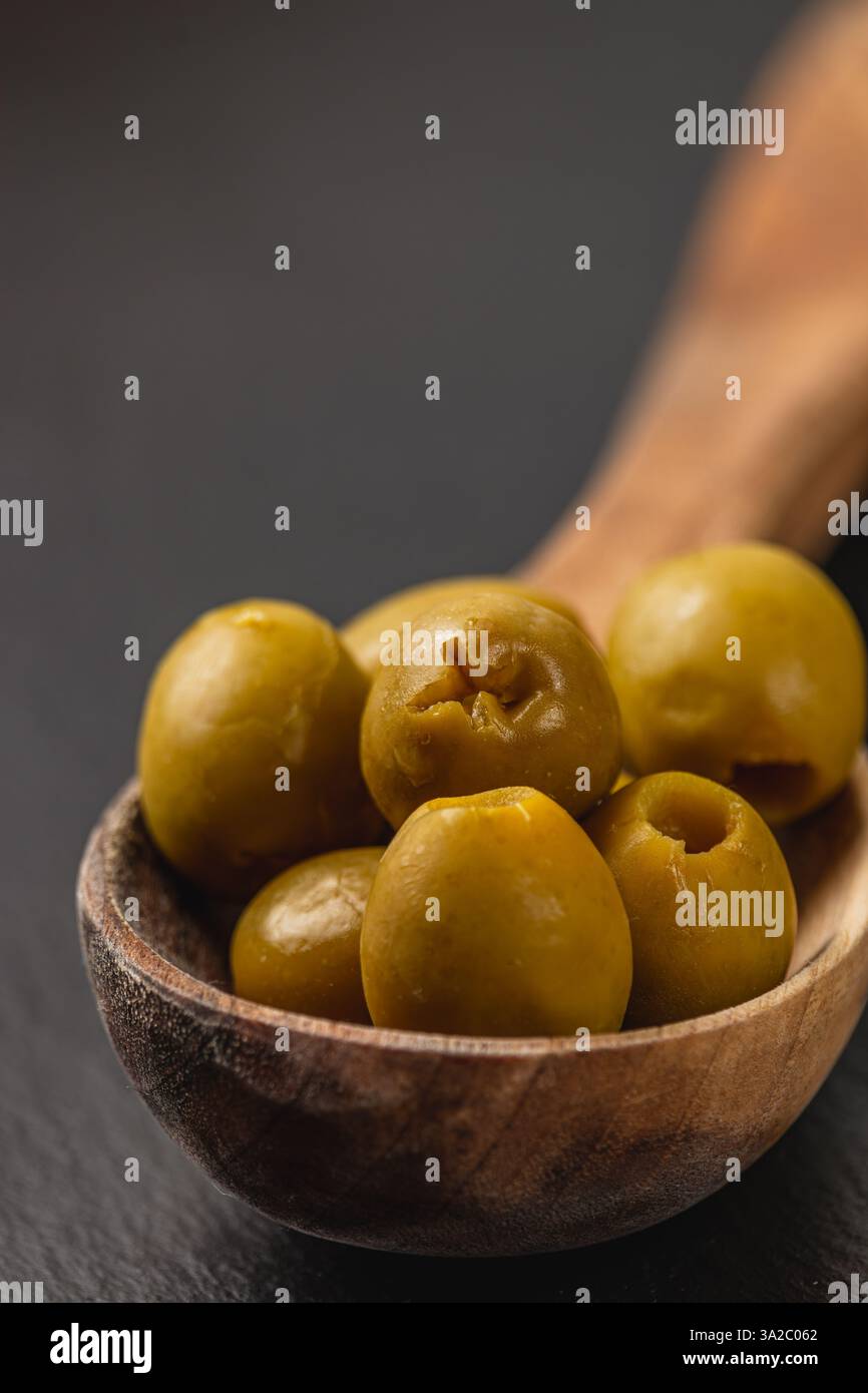 Une collection d'olives vertes remplit un bol en bois sculpté, mettant en valeur leur texture brillante. Le fond sombre souligne la riche couleur verte et l'orga Banque D'Images