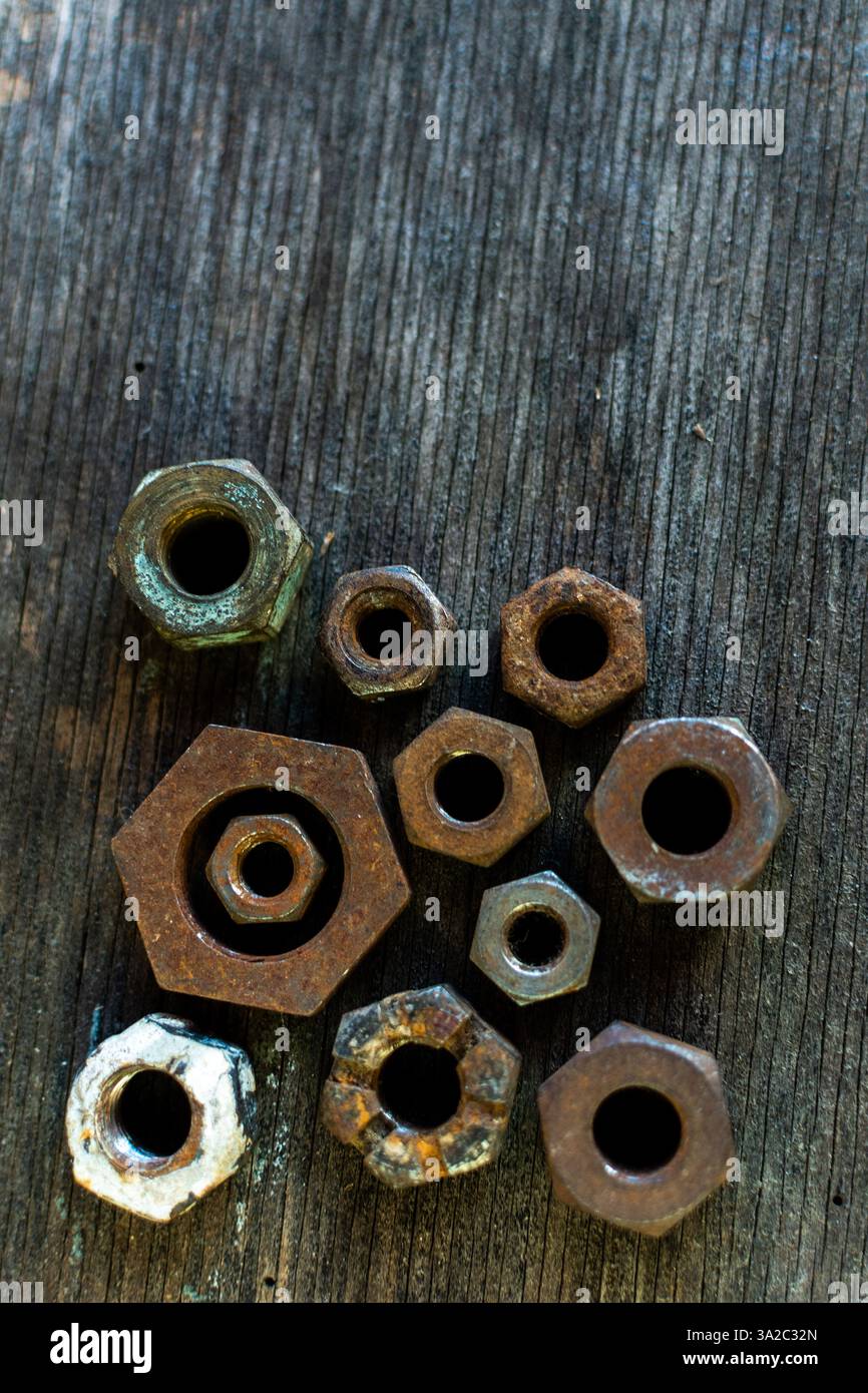 Collection d'écrous en métal rouillé disposés sur une surface en bois altérée mettant en valeur des textures et des formes uniques Banque D'Images