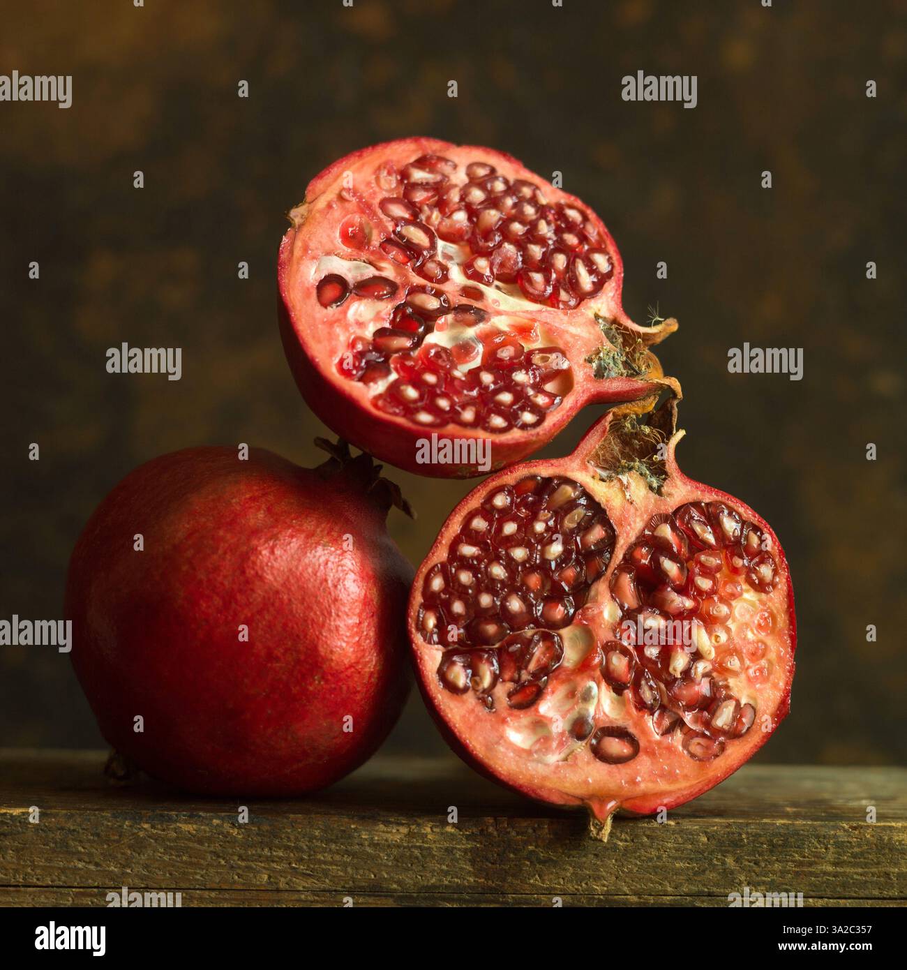 Grenades coupées en deux avec des graines exposées sur une surface en bois dans un éclairage doux Banque D'Images