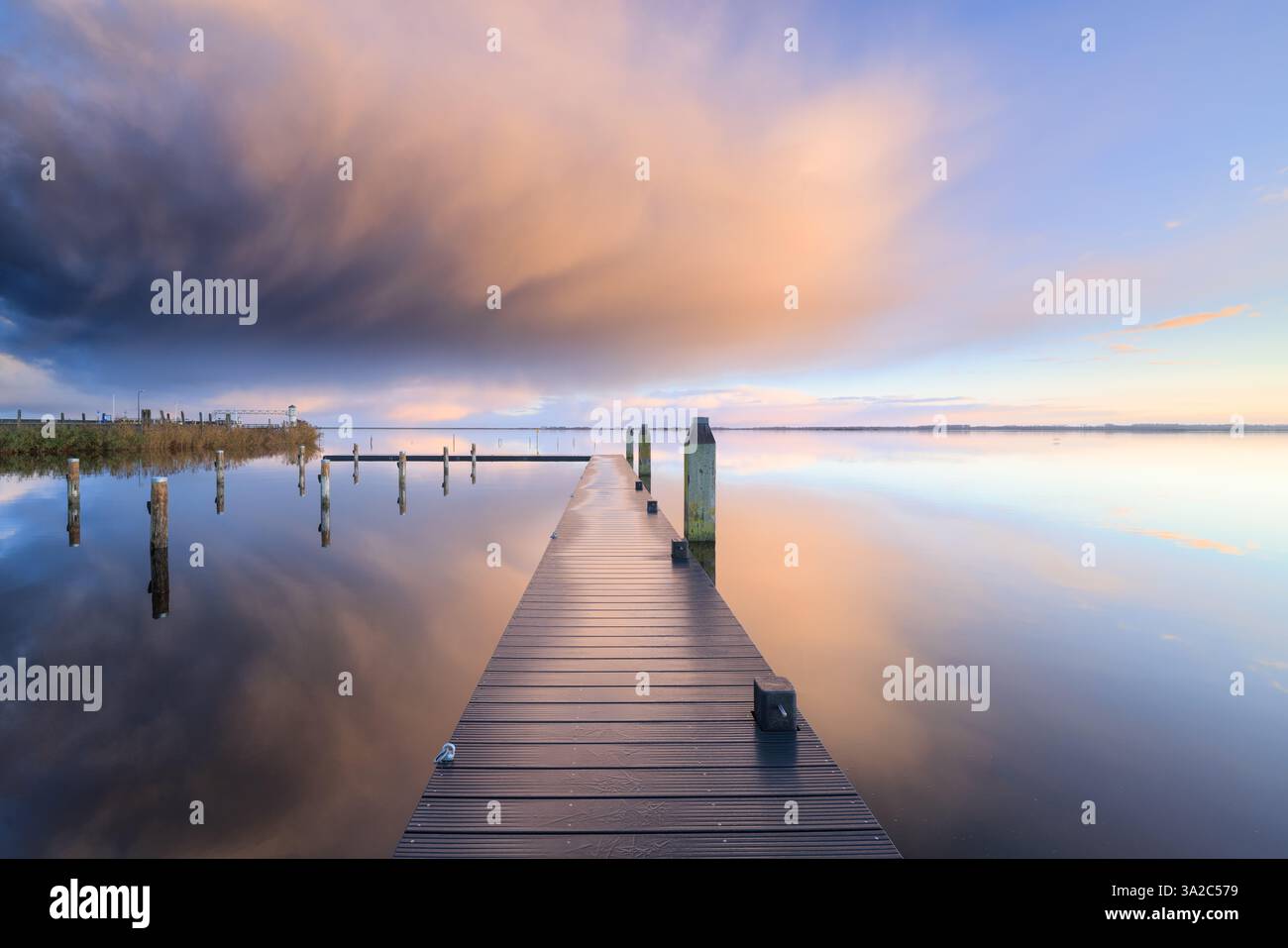 Un reflet parfait des nuages orageux dans le lac Lauwersmeer aux pays-Bas avec un quai menant à l'horizon. Banque D'Images