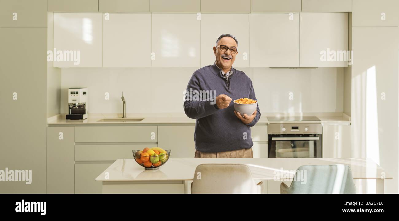 Homme mûr souriant tenant un bol de céréales dans une cuisine Banque D'Images Homme mûr souriant tenant un bol de céréales dans une cuisine Banque D'Images