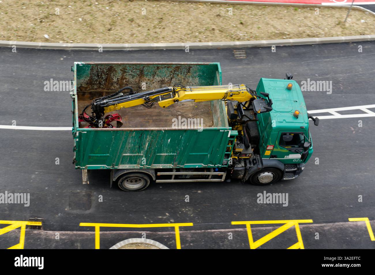 l'image montre un camion vert avec un conteneur vide et un bras hydraulique jaune, probablement utilisé pour la collecte des déchets ou la construction Banque D'Images