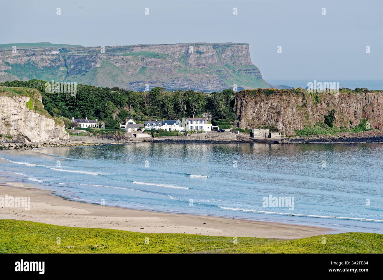 White Park Bay sur la côte nord d'Antrim, Irlande du Nord. Les falaises de basalte de la chaussée des géants s'élèvent derrière le village de pêcheurs de Portbradden Banque D'Images