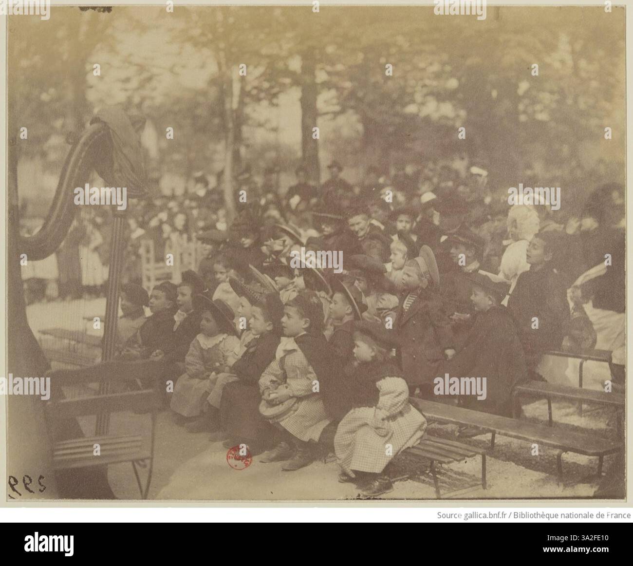 La photographie d’Eugène Atget représente un spectacle de marionnettes de Guignol au jardin du Luxembourg, offrant un aperçu des loisirs et des divertissements parisiens du début du XXe siècle. Banque D'Images
