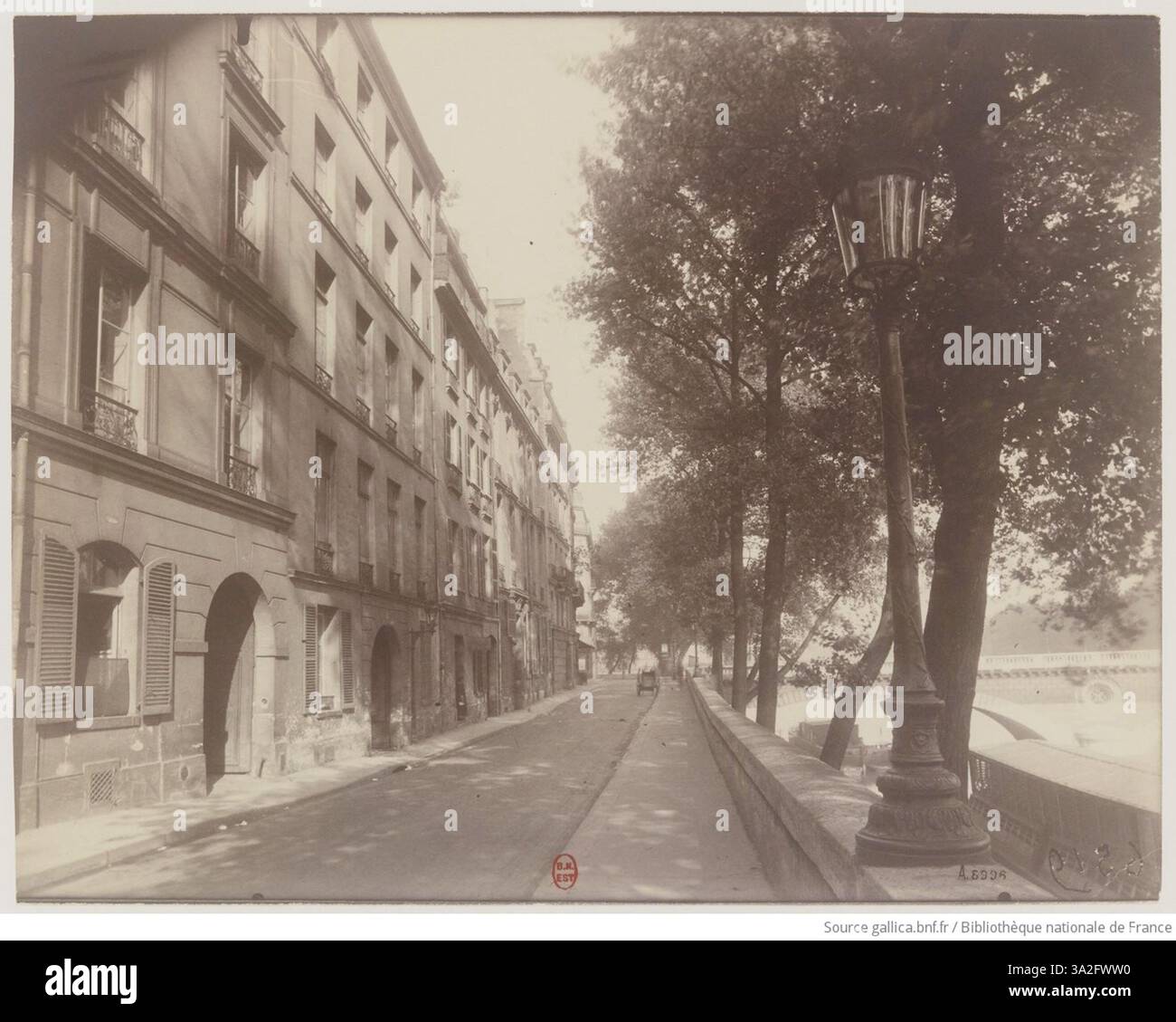 Dans cette photographie, Eugène Atget capture le Quai Bourbon à Paris à l'aube du mois d'août. L'image se concentre sur la scène tranquille de la rivière, mettant l'accent sur les éléments architecturaux le long du quai. Banque D'Images