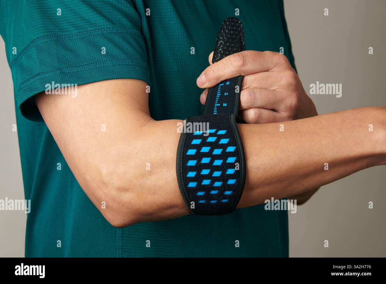 un homme, portant un t-shirt de sport vert, ajuste son bracelet d'épicondylite sur son bras, pour soulager la douleur de l'épicondylite, également connue sous le nom de tennis elbow Banque D'Images