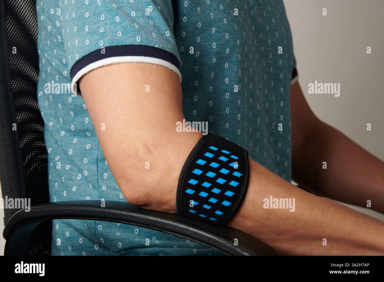 un homme porte un bracelet d'épicondylite sur son bras, pour soulager la douleur de l'épicondylite, alors qu'il est assis à son bureau Banque D'Images