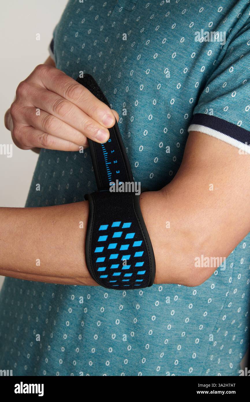 un homme ajuste son bracelet d'épicondylite sur son bras, pour soulager la douleur de l'épicondylite, également connu sous le nom de tennis elbow Banque D'Images