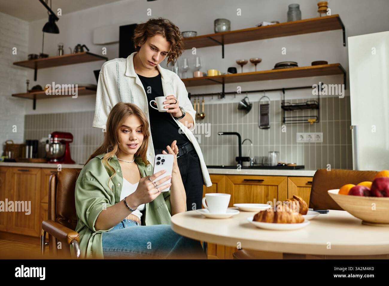 Jeune couple se détend ensemble dans une cuisine moderne, partageant des rires et un moment chaleureux autour d'un café. Banque D'Images