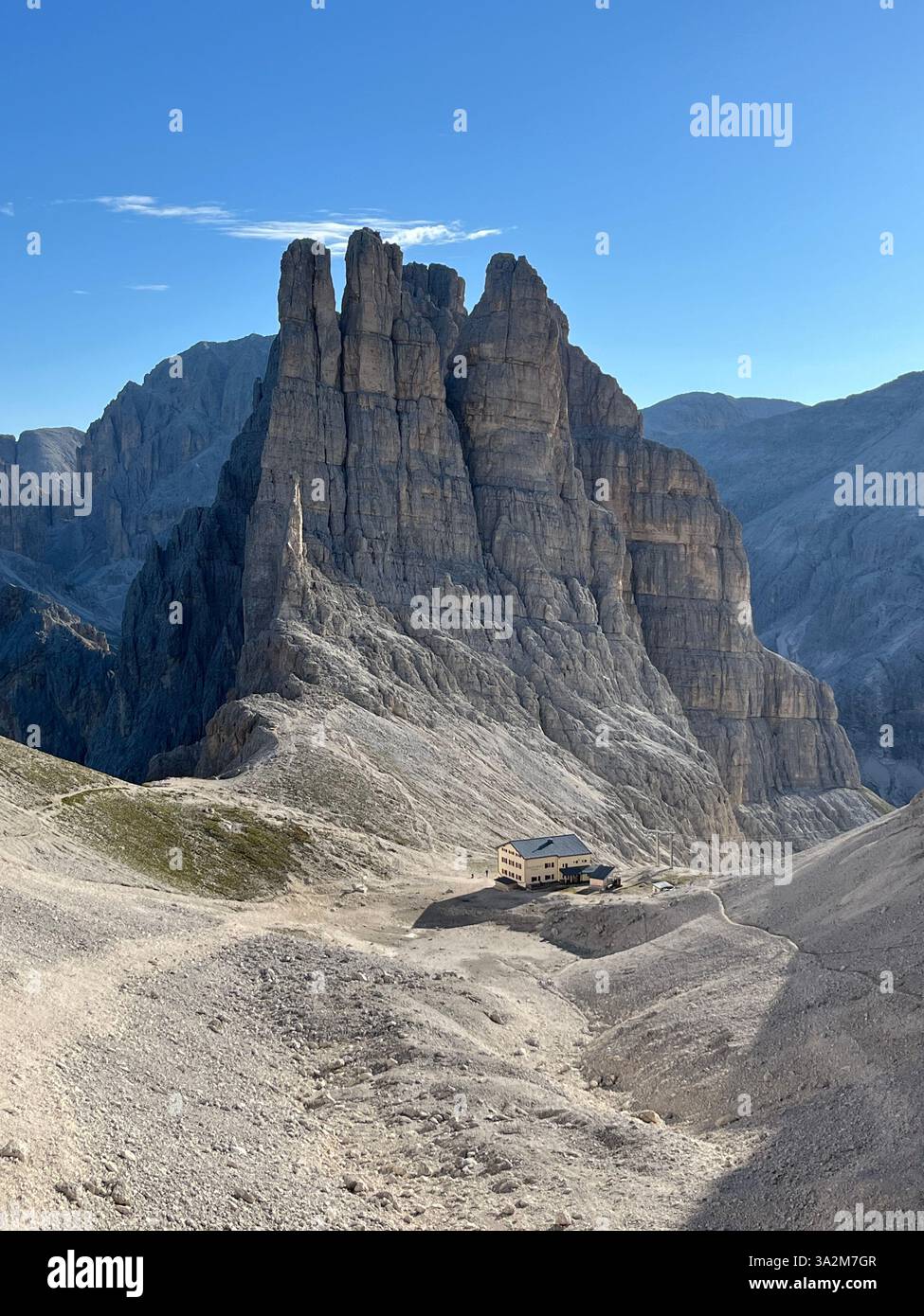 Légende : une cabane de montagne isolée nichée dans les Dolomites accidentées, entourée d'imposantes formations rocheuses sous un ciel bleu clair. Banque D'Images