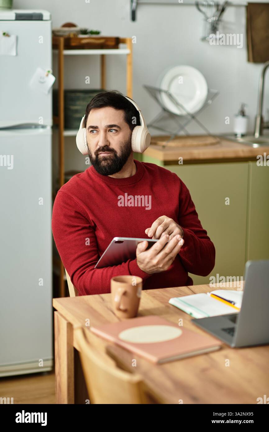 Un homme âgé élégant en tenue décontractée aime la musique avec des écouteurs tout en tenant une tablette. Banque D'Images