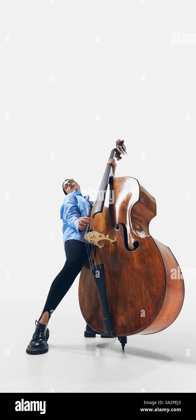 Bassiste féminine jazz élégante avec de longs cheveux coulants, embrassant le son et le rythme dans une expression musicale puissante sur fond blanc. Banque D'Images