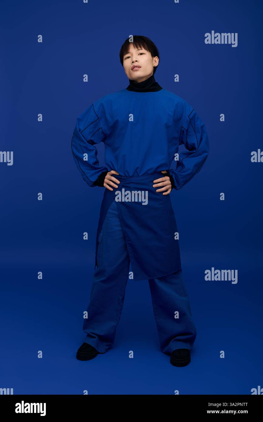 Confiant jeune homme asiatique pose avec les mains sur les hanches, affichant sa tenue bleue frappante. Banque D'Images