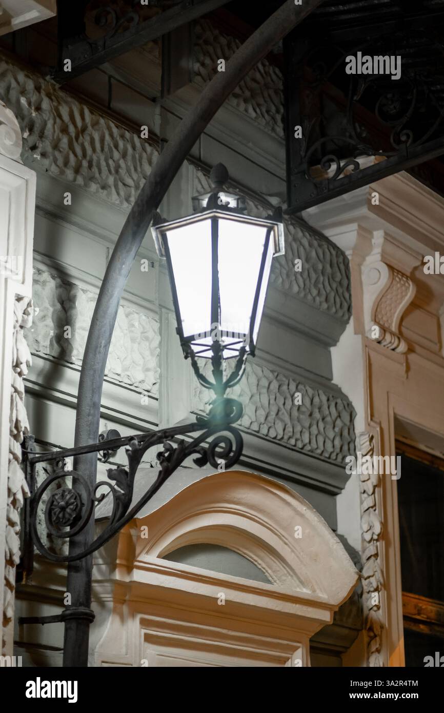 Un lampadaire vintage jette une lumière chaude sur la façade complexe d'un bâtiment historique à Saint-Pétersbourg, créant une atmosphère enchanteresse après le soleil Banque D'Images