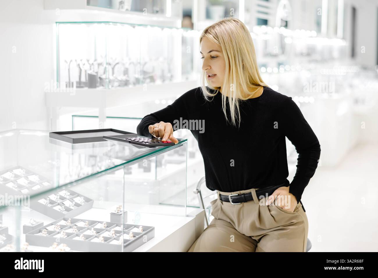 Jeune vendeuse calcule le prix des bijoux à l'aide d'une calculatrice dans une bijouterie Banque D'Images