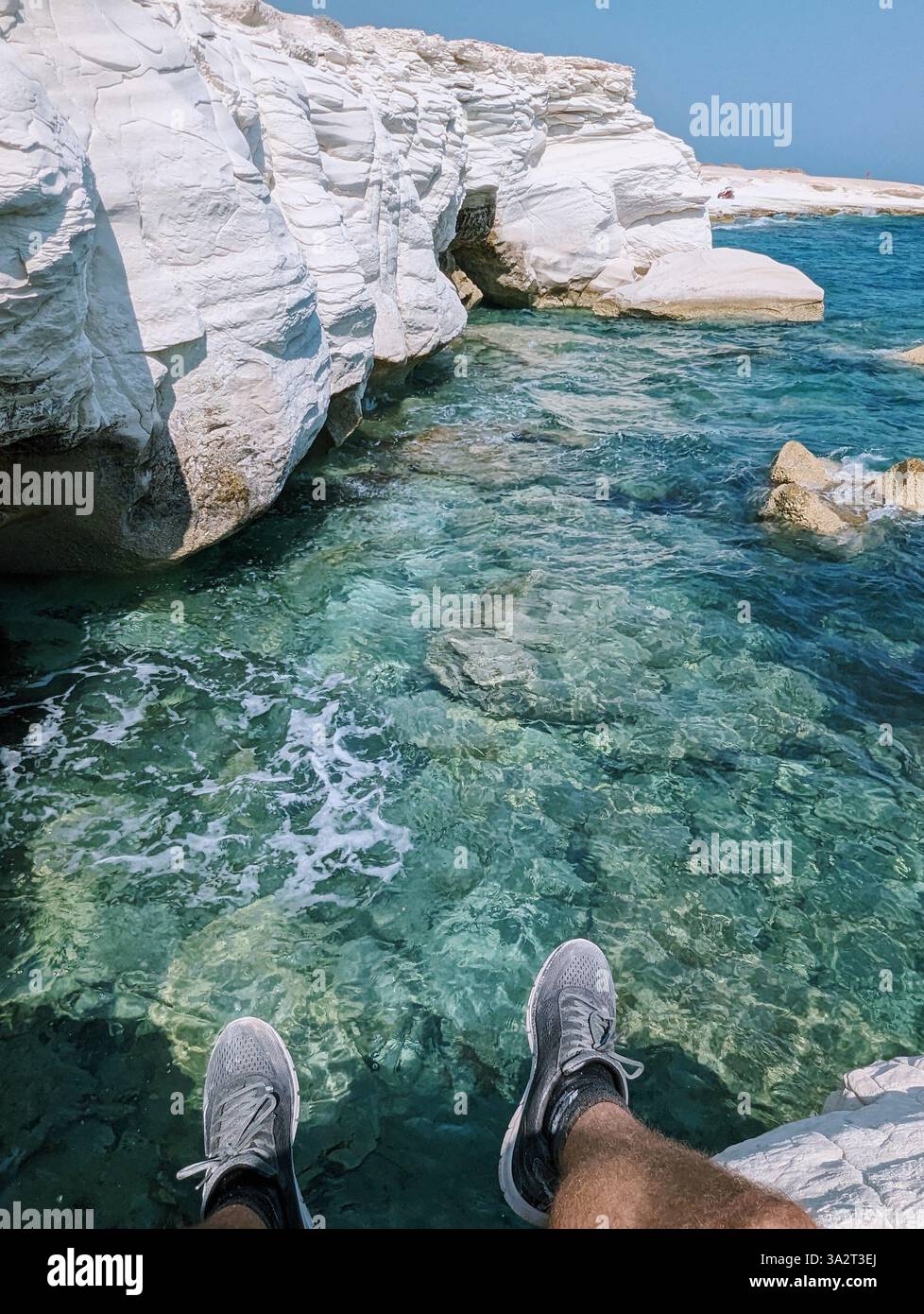 Les pieds pendent au-dessus du baiser turquoise de Chypre, où les falaises blanches rencontrent le bonheur serein de la mer. Governor's Beach murmure, 'juste respirer'. - Image de stock capturée avec un smartphone