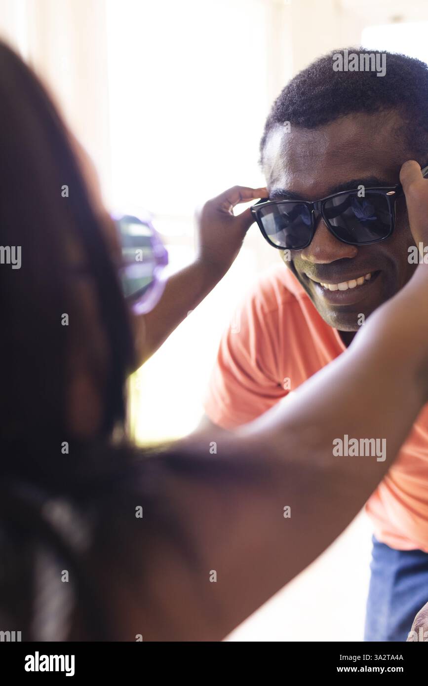 Père afro-américain et enfant jouant avec des lunettes de soleil à la maison, partageant des moments joyeux ensemble Banque D'Images