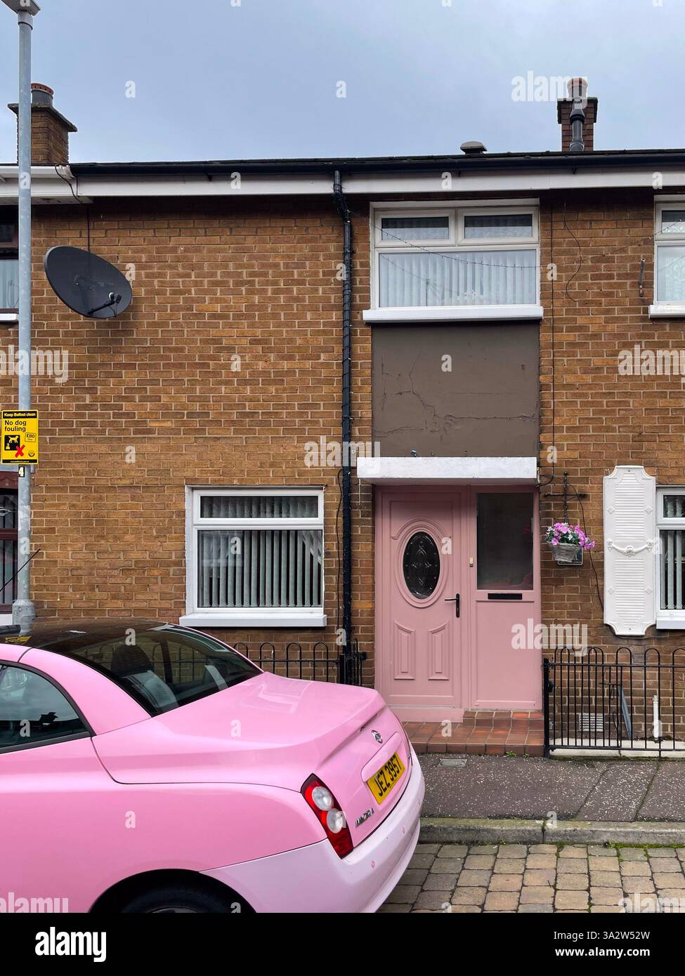 Une voiture rose pastel garée devant une porte rose assortie à Belfast, en Irlande du Nord. Banque D'Images
