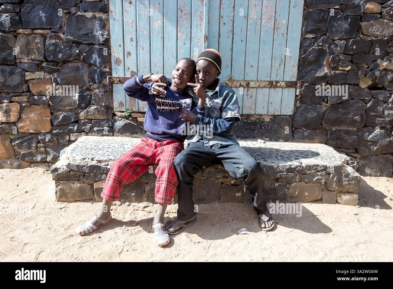 Dakar, Sénégal – deux garçons de l’île de Gorée partagent un moment ludique sur un banc de pierre, offrant un aperçu de l’enfance sur cette île historique. Banque D'Images