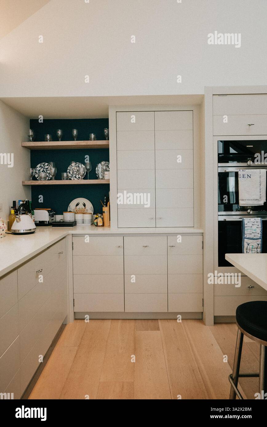 Une cuisine avec des armoires blanches et un mur bleu. Les armoires sont pleines de vaisselle et de verres. La cuisine a un look propre et organisé Banque D'Images