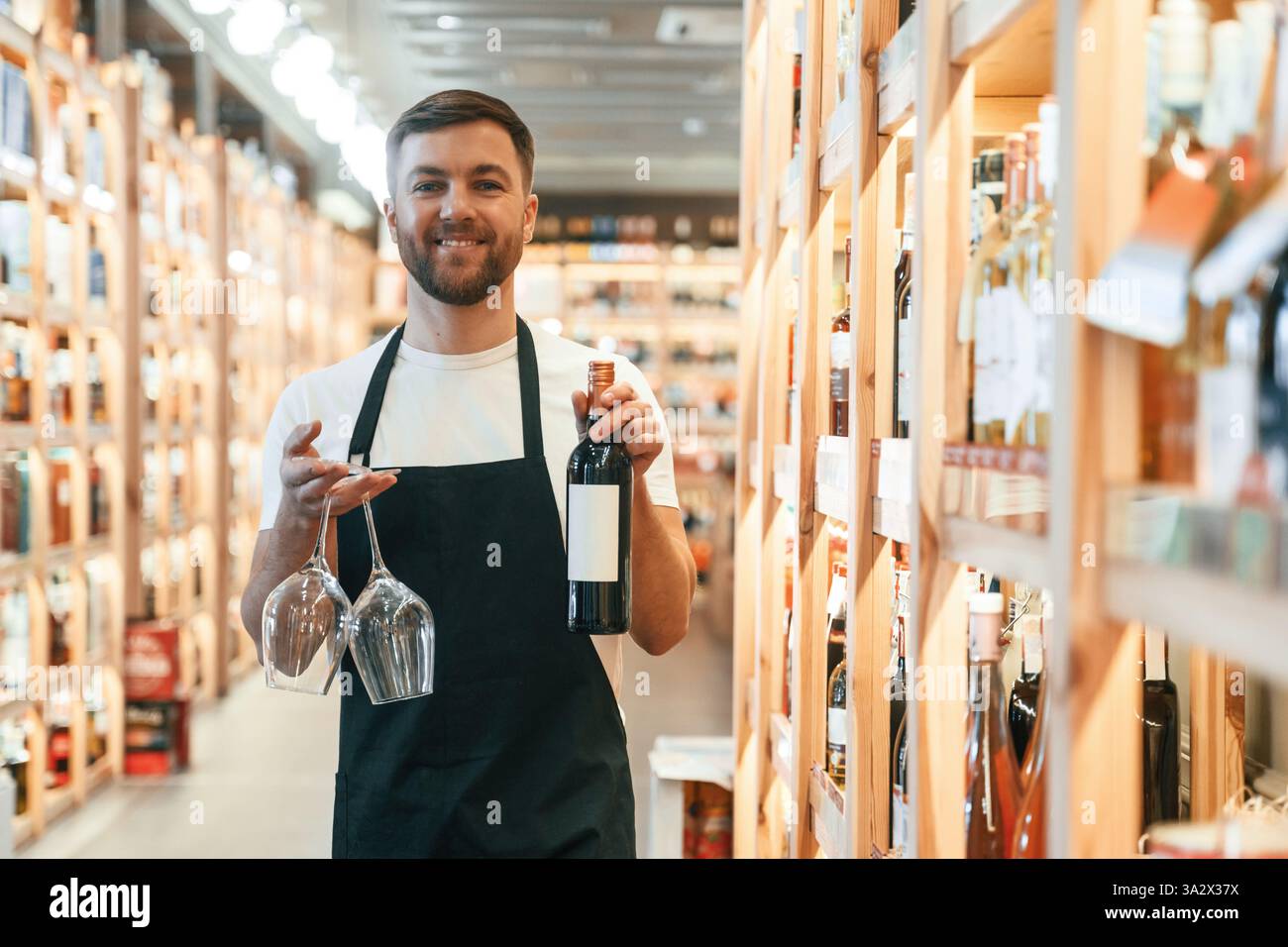 Deux verres et bouteille dans les mains. Propriétaire d'un magasin de vin en chemise blanche et tablier noir. Banque D'Images